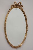 20th century oval gilt wood and gesso framed bevel edged mirror, floral decoration, bow pediment,