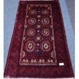 Persian Baluchi red ground rug, repeating gul design, with purple elements,