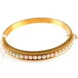 A good Victorian matte gold bangle, half of the hoop is set with pearls in a gold bead border,