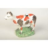 An early 19th century cow creamer with red and black markings on shaped, rectangular green base.