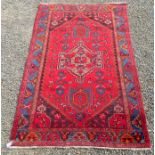 A Hamadan rug, the red field with a large central pole medallion and blue gul border, 190 x 125cm.