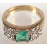 A 9ct. gold ring with a square cut emerald flanked by diamond clusters.