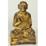 A gilt bronze figure of a monk or Buddhist priest seated upon two cushions,