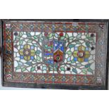 A leaded coloured glass panel with central shield flanked by flowers and tendrils,