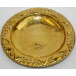 A brass Arts and Crafts European dish with a fruit decorated repousse rim and planished centre,