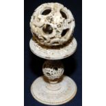 A Chinese ivory puzzle ball and stand, the ball carved with dragons and clouds,