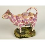 An early 19th century pink lustre cow creamer with saddle, horns chipped.