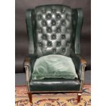 A buttoned green leather upholstered wing armchair.
