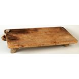 A pine bread board on four legs, at one end, a handle.