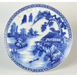 A Japanese Arita blue and white charger, decorated with a riverside scene,