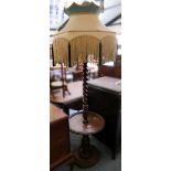A carved wooden standard lamp, with barley twist stem and undertier with yellow fringed shade