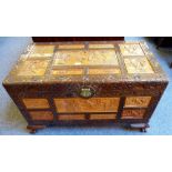 A Chinese camphor wood chest, inset with carved sandalwood panels of figures and buildings on