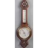 An aneroid barometer and thermometer with silvered dial, contained in a carved oak wheel case