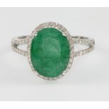 A 14ct white gold oval emerald and diamond cluster ring, the centre stone approx 4ct surrounded by