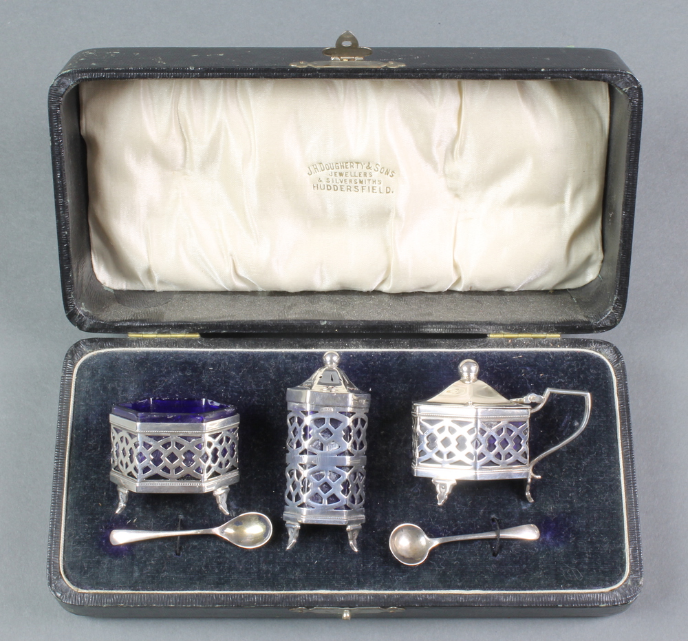 A silver 3 piece hexagonal condiment set with pierced decoration and blue glass liners, together