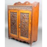 An Edwardian Art Nouveau carved oak hanging smokers cabinet with raised back, enclosed by panelled