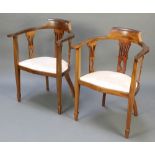 A pair of Edwardian mahogany slat back open arm chairs with pierced backs, raised on square tapering