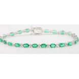 An 18ct white gold emerald and diamond line bracelet with 24 oval cut emeralds interspersed with