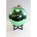 AN EARLY 20TH CENTURY GREEN GLASS WITCH BALL, 9 ins diameter with a non-contemporary stand.