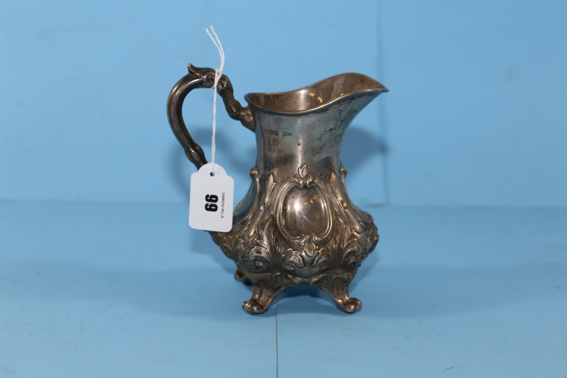 AN EDWARDIAN SILVER CREAM JUG of waisted circular form with floral embossing and scroll feet,