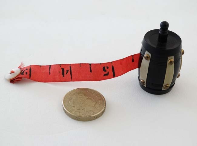 Sewing / Needlework : A tape measure formed as an ebonised barrel with ivorine banding held by