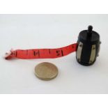 Sewing / Needlework : A tape measure formed as an ebonised barrel with ivorine banding held by