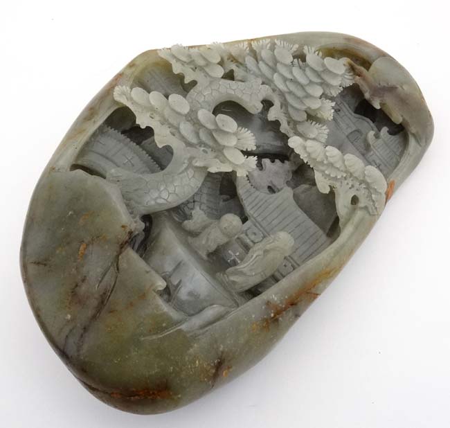 A large jade carving depicting figure of a sage and scholar with temples amongst spruce trees.