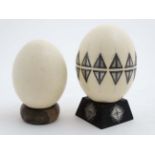 Two ostrich eggs one with applied decoration and approx 8" high ( including stand )