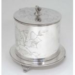 A silver plated biscuit barrel with hinged lid and three scrolled feet .