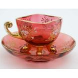 A 20thC cranberry glass cup and saucer with white enamel and gilt decoration 5 1/2" wide