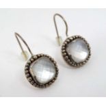 A pair of silver drop earrings set with facet cut moonstone style stones within beaded borders.