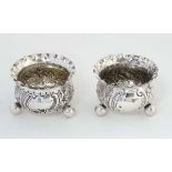 A matched pair of silver salts with embossed foliate decoration and three ball feet.