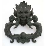 A cast bronze door knocker in the form as a green man with two caryatid and cherub formed knocker.