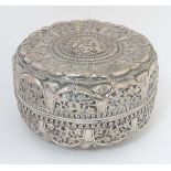 A white metal box and cover of circular form with profuse foliate decoration and central image to