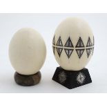 Two ostrich eggs one with applied decoration and approx 8" high ( including stand )