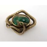 A yellow metal brooch with central hardstone cabochon bordered by a snake formed mount with emerald