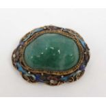 A late 20thC Oriental brooch with central jade like stone in a gilt metal mount with enamel