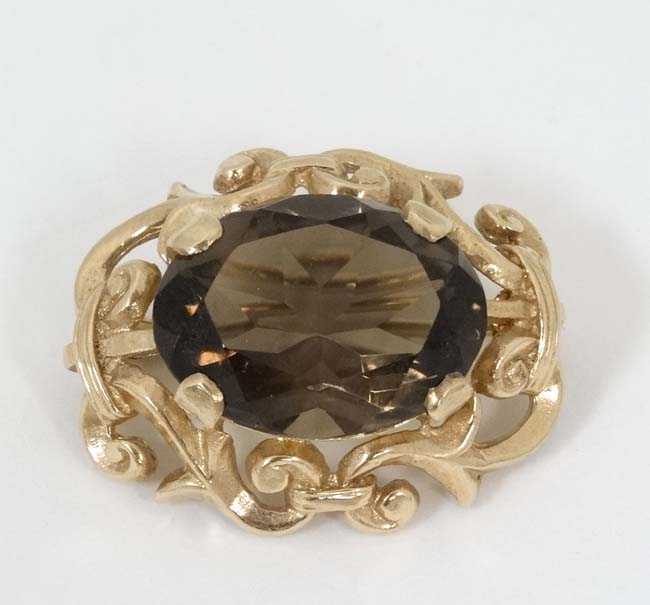 A 9ct gold brooch set with central facet cut smokey quartz within a scrolling mount.