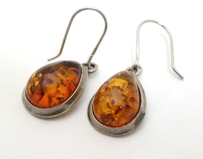 A pair of silver and white metal drop earrings set with amber.