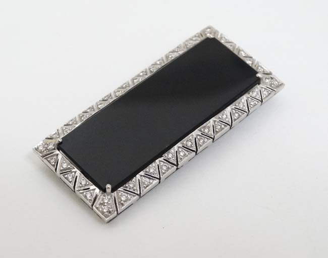 An unusual Art Deco style brooch set with central black onyx surrounded bordered by diamonds in a