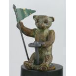 *Theodore the Teddy Bear, holding a steering wheel with one hand and a flag-staff with the other,