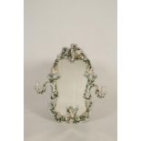 A DRESDEN STYLE FLORAL AND CHERUB ENCRUSTED WALL MIRROR, the shaped plate within a scrolling