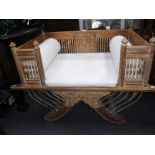 AN ORIENTAL STYLE DAY BED with carved and bobbin-turned three-quarter surround on 'X'-shaped base