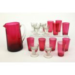 Victorian cranberry glass jug, nine cranberry glass beakers and six Victorian penny shot glasses,