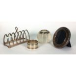 Silver items comprising six slice toast rack, glass match striker, circular photo frame and a napkin