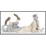 A large Lladro figure of a clown in repose leaning with his foot resting on a large circus ball.