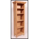 A tall contemporary stripped light pine upright bookcase cabinet with flared top and fixed shelves.