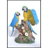 A highly detailed resin parrot figurine group perched atop a tree trunk on resin base set in
