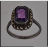 A white metal dress ring set with a central emerald cut amethyst stone surrounded by a halo of