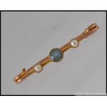 An Edwardian yellow metal bar brooch set with an aquamarine and two seed pearls.